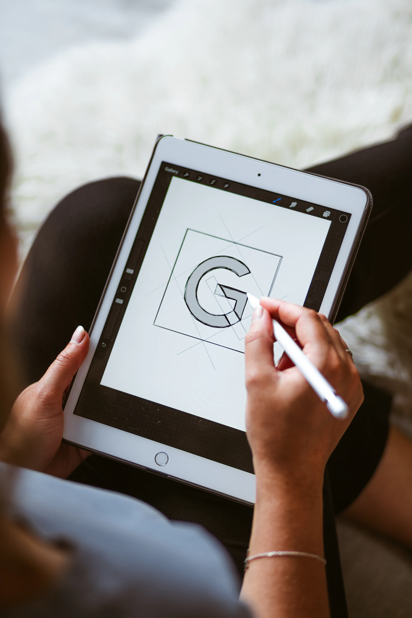 A hand using a stylus to develop a geometric letter sketch on a tablet
